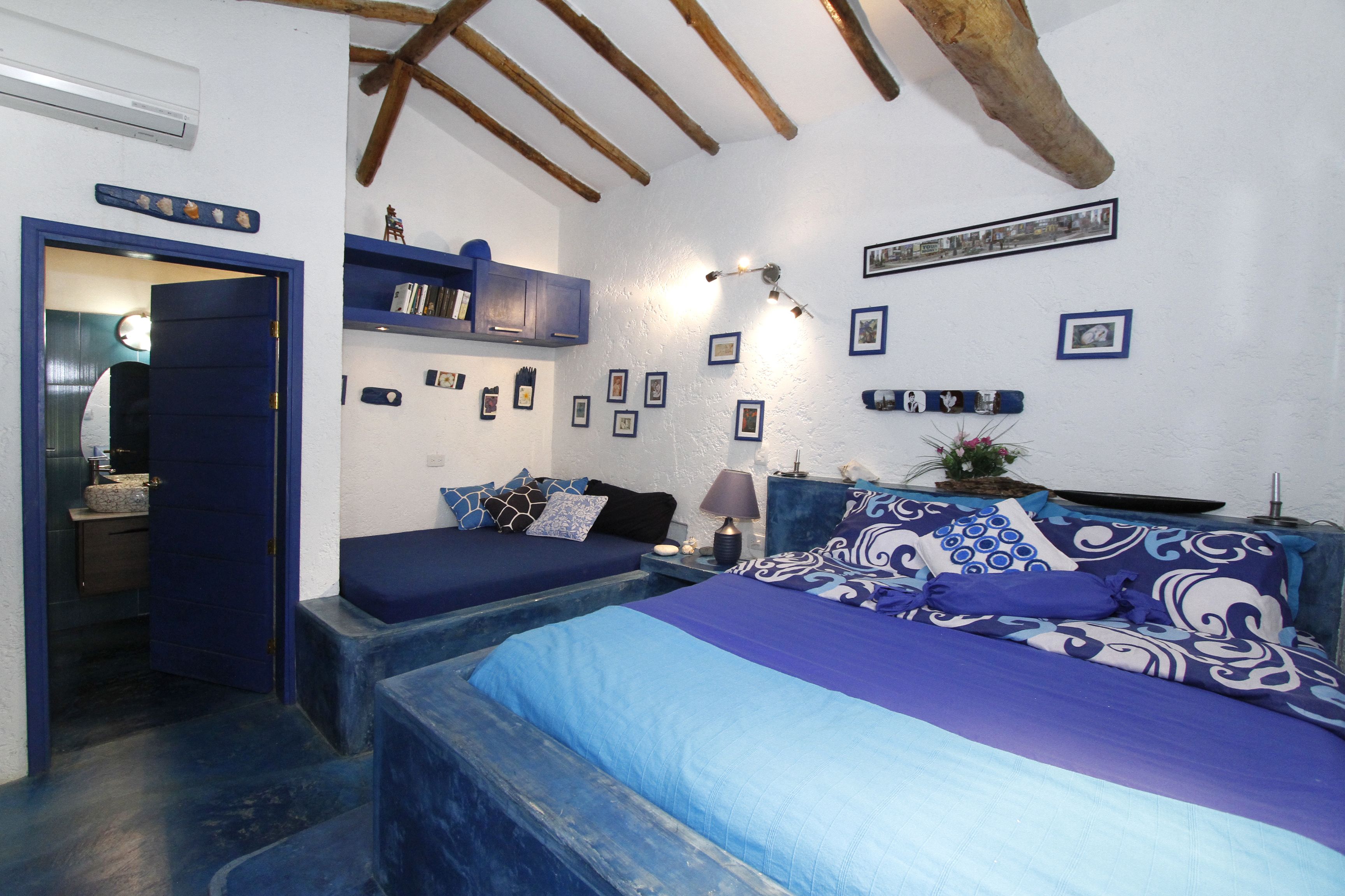 A bedroom with two beds, a wooden ceiling, and a wall decorated with framed pictures.