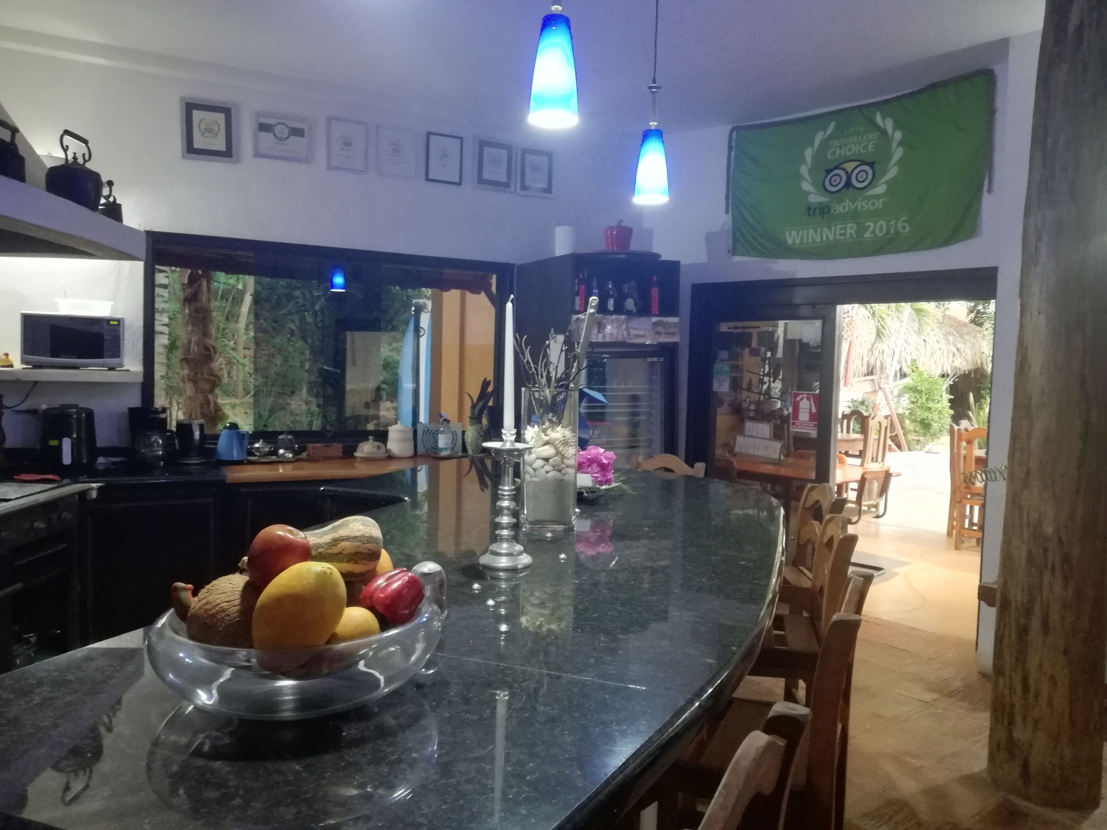 A kitchen with a large island, a microwave, and a coffee maker. There is a bowl of fruit on the island.