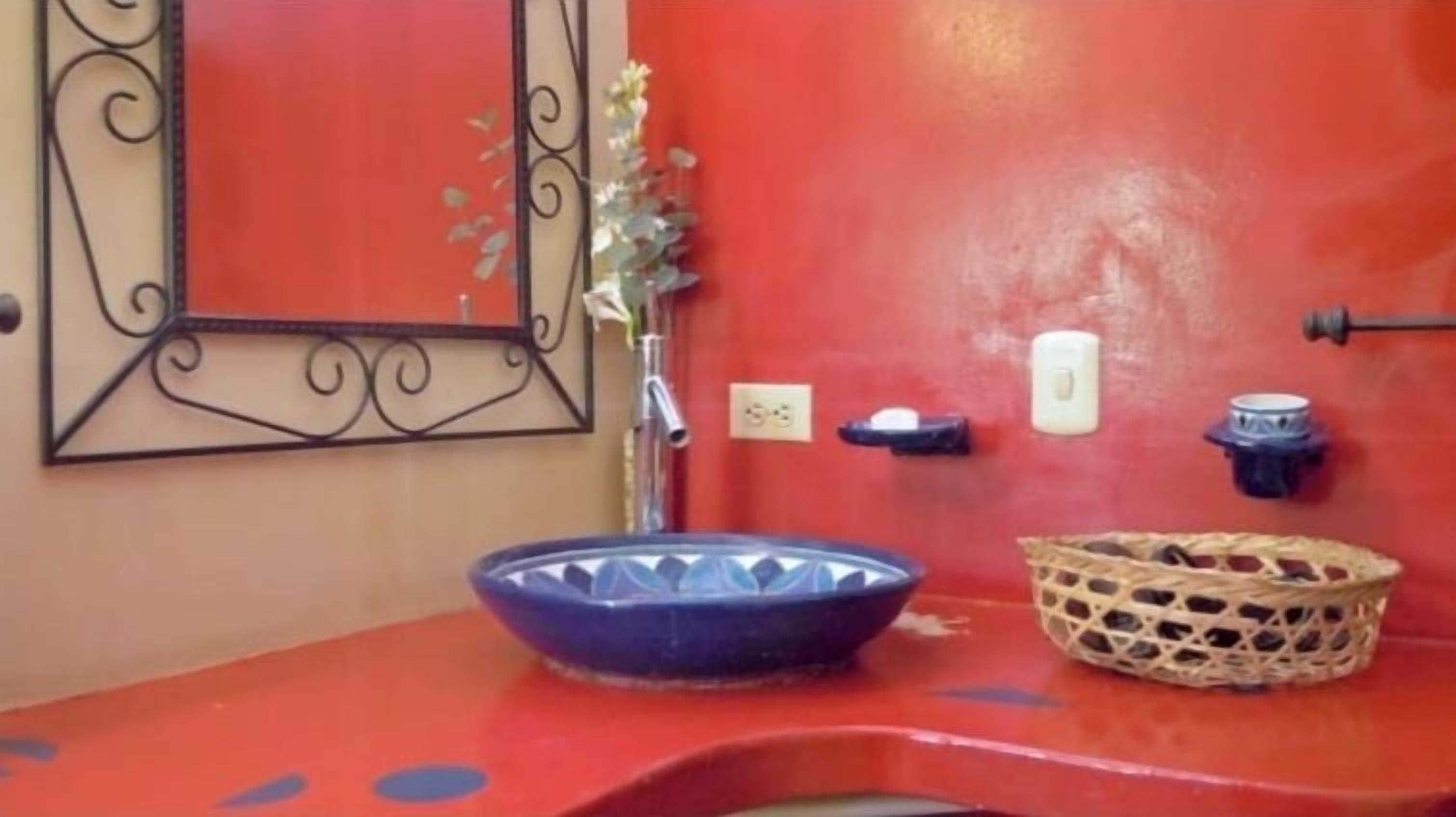 Un bagno con un lavabo blu, un cesto in vimini, un interruttore a muro e uno specchio decorativo.