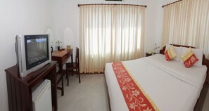 A hotel room with a bed, a desk with a television, a chair, and curtains. - Xing Angkor Hotel (Siem Reap)