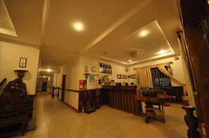 A reception area with a wooden reception desk, a clock, and framed pictures on the wall. - Xing Angkor Hotel (Siem Reap)
