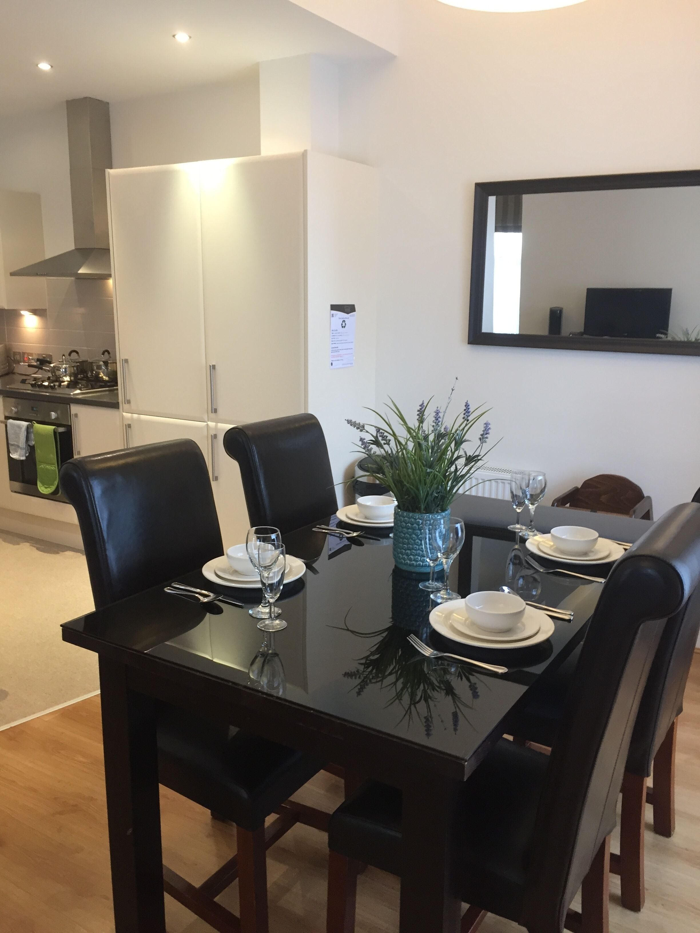 Een moderne eethoek met een glazen tafel, zwarte stoelen en een blauwe vaas als middelpunt.