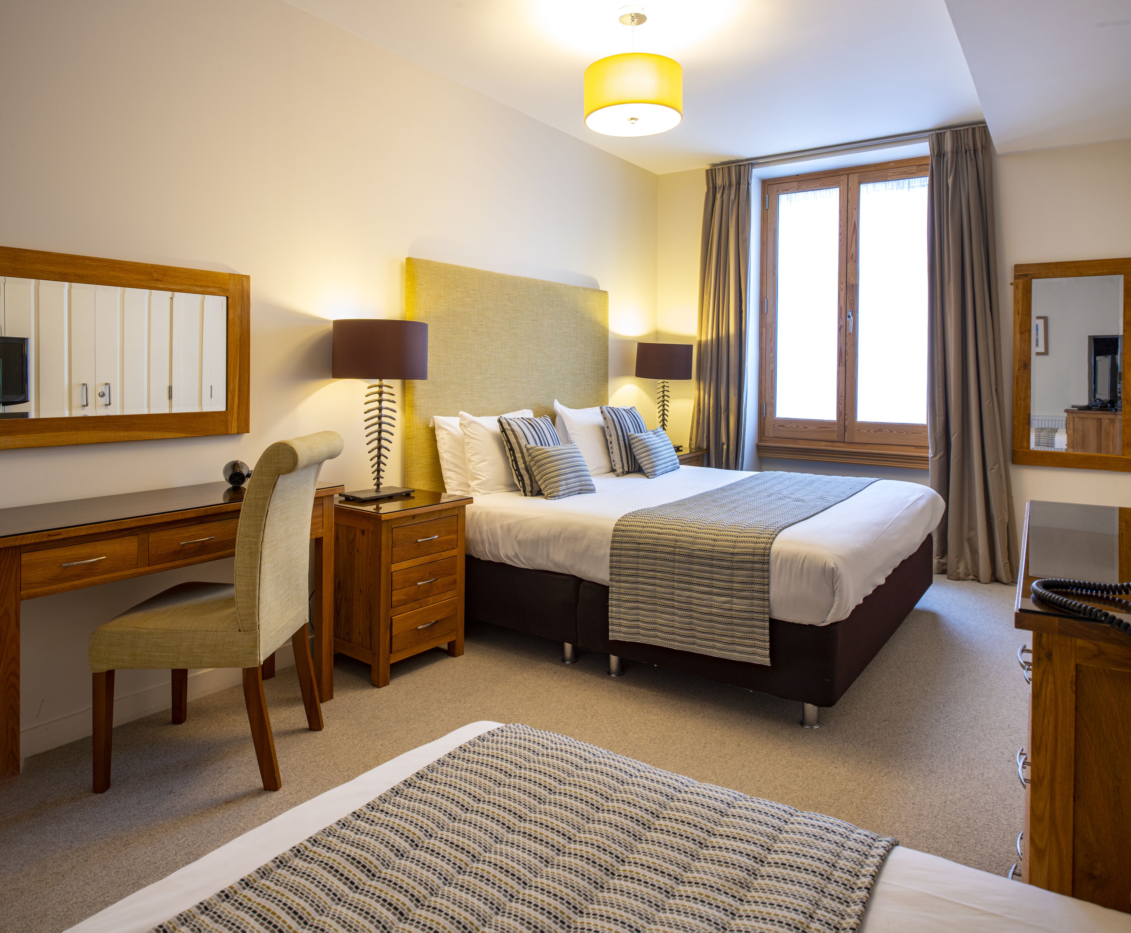 A hotel room with a bed, desk, chair, and a large window with curtains.