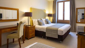 A hotel room with a bed, desk, chair, and a large window with curtains.