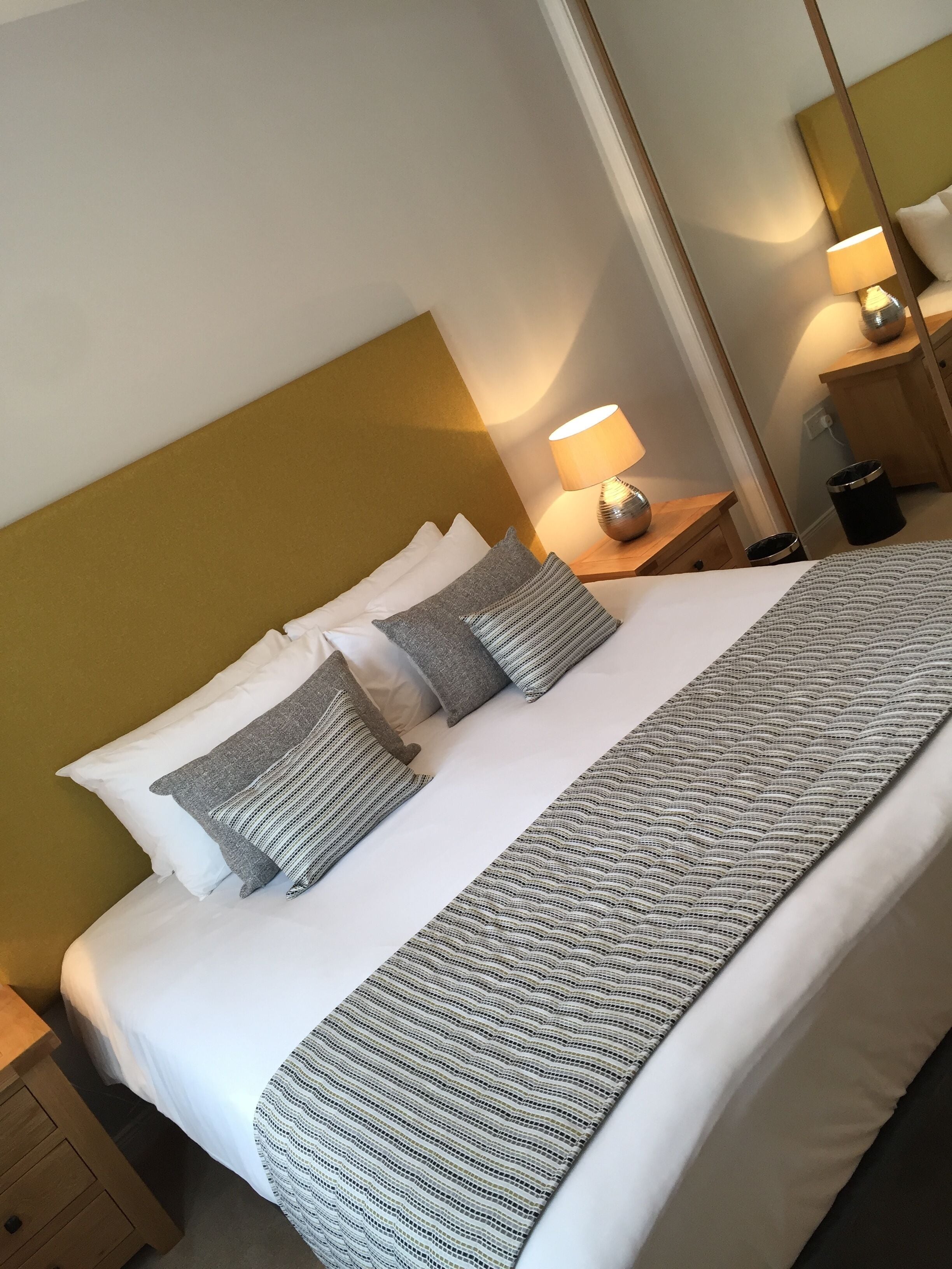 A neatly made bed with white and gray striped bedding, a wooden headboard, and a bedside lamp.