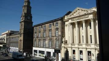 A street view with a clock tower, a building with classical architecture, and a white van parked on the side.