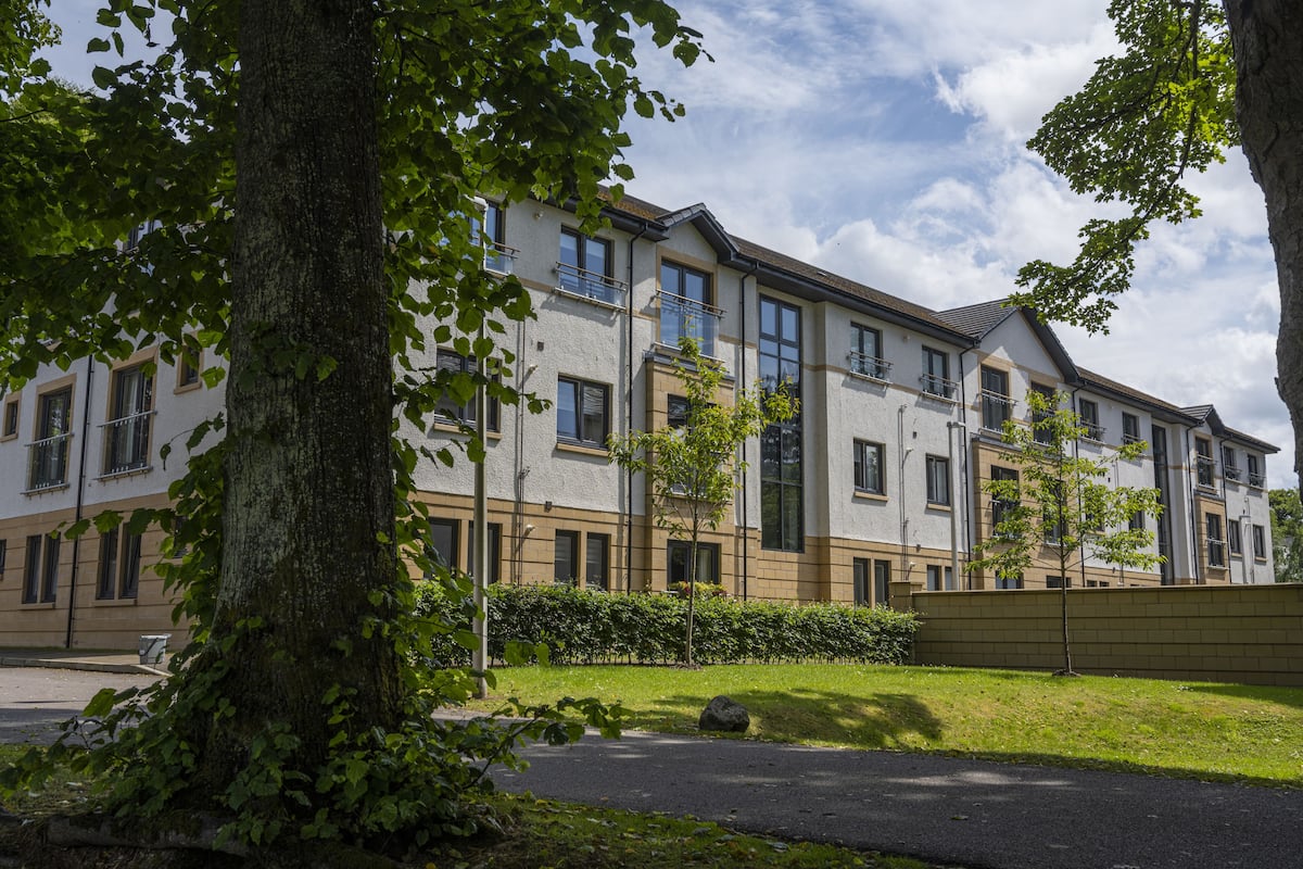 A multi-story residential building with balconies, a paved driveway, and a well-maintained lawn.