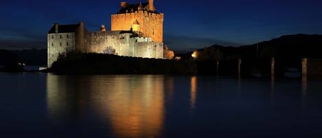 A historic castle with a moat, illuminated by lights at night.