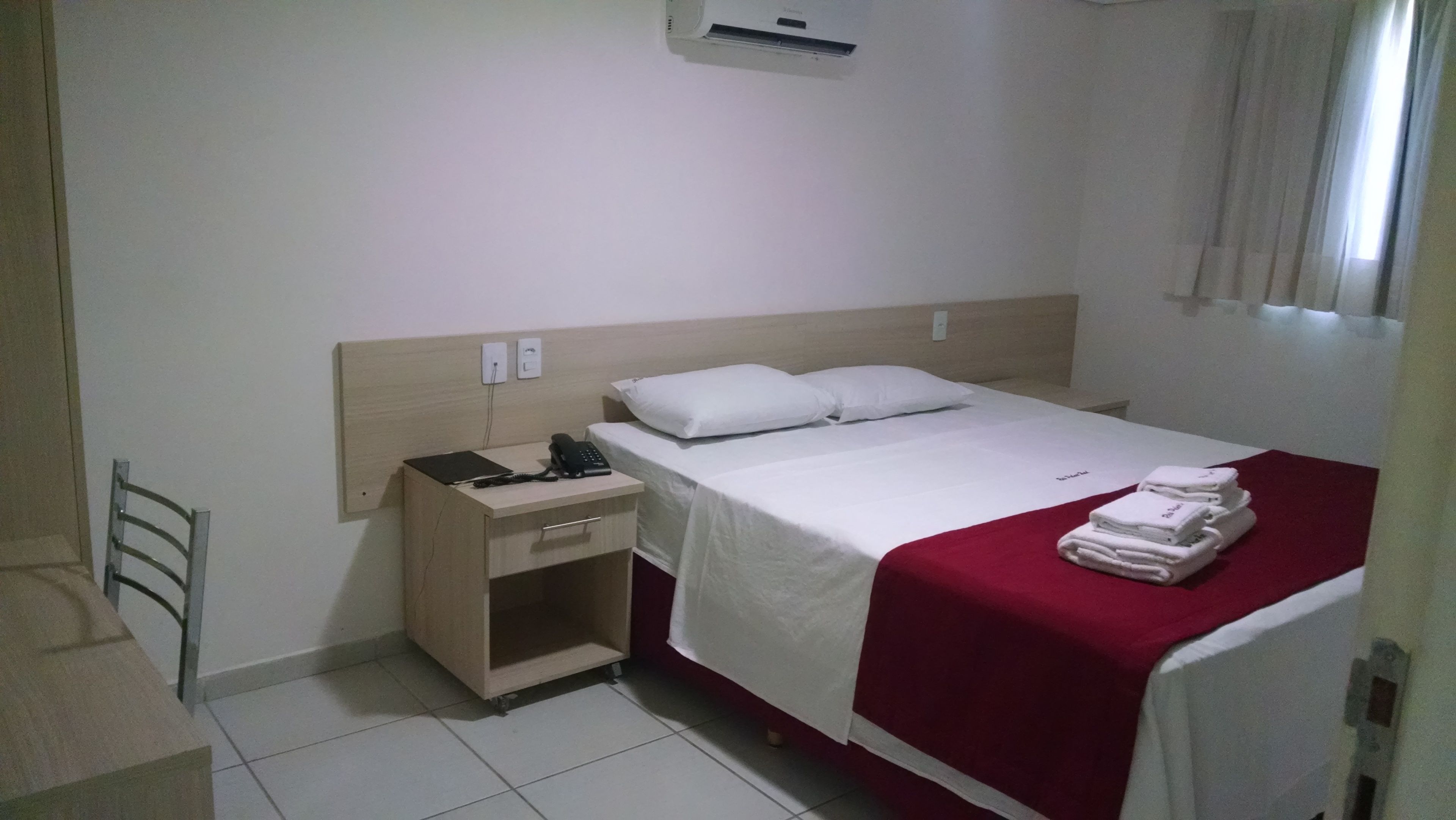 Une chambre d’hôtel avec un lit, un bureau doté d’un téléphone et un appareil de climatisation fixé au mur.