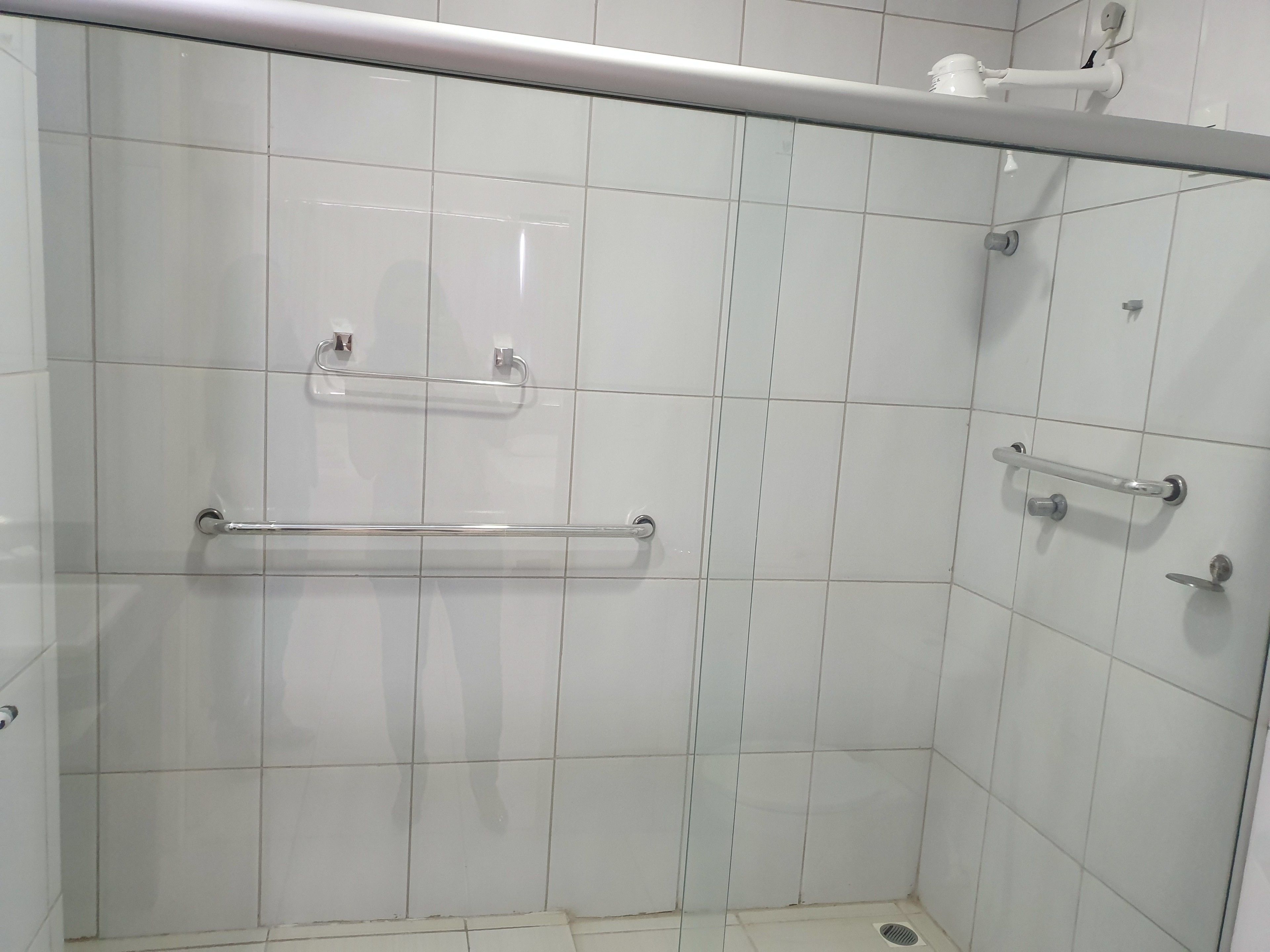 A walk-in shower with white tiles, a glass door, and a metal grab bar.