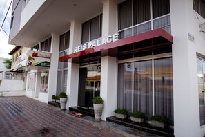 Welcome to the Reis Palace, featuring a modern entrance with large windows and a clean facade, surrounded by lush greenery.