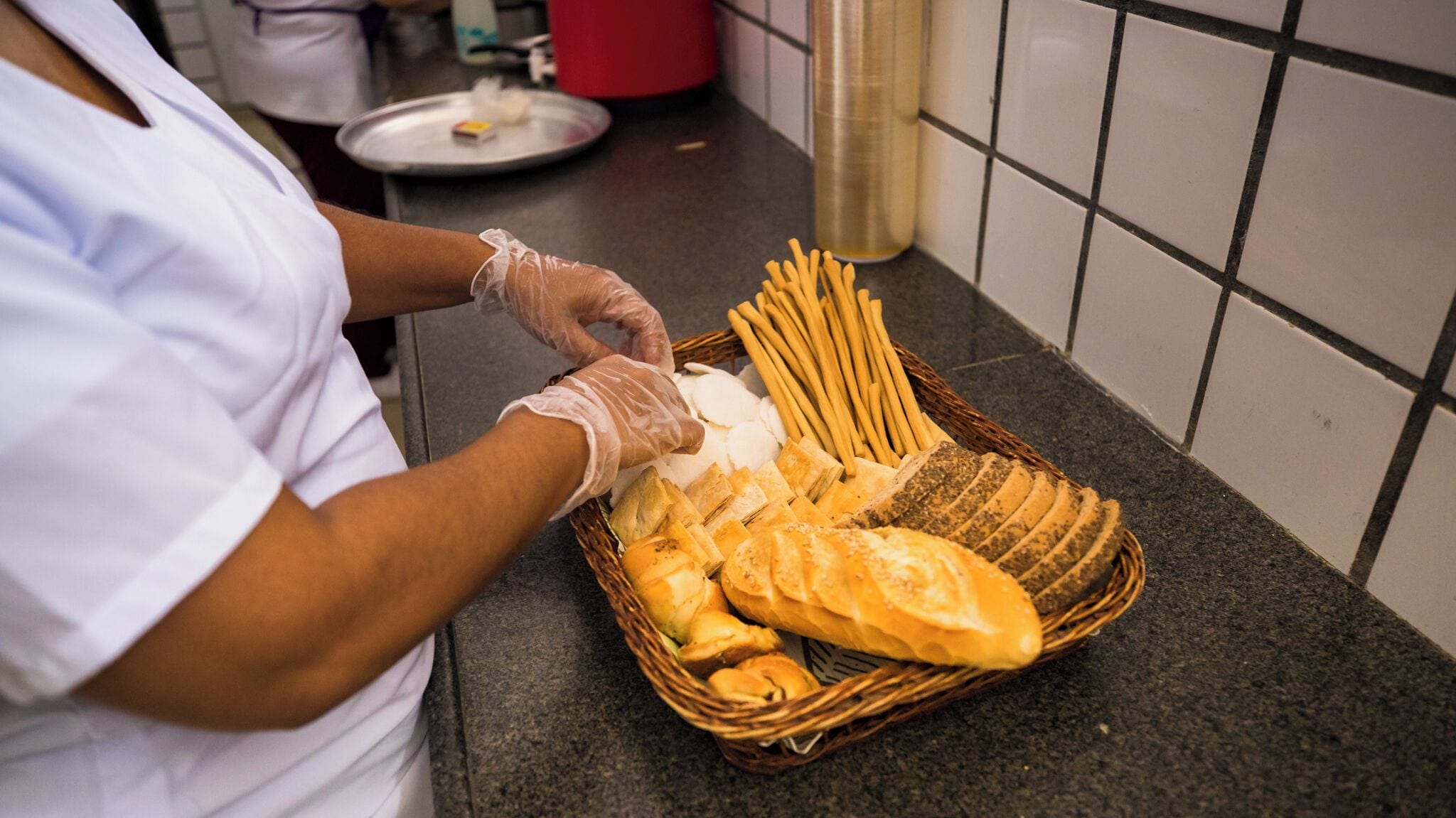 A person in a white uniform handling bread and baguettes on a kitchen counter.