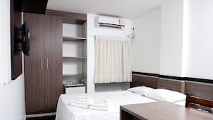 A hotel room with a bed, a desk, a wardrobe, a TV, a shelf with toiletries, and an air conditioning unit. - Reis Palace Hotel (Petrolina)