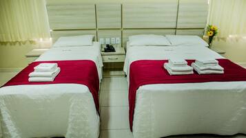 A hotel room with two beds, each with a red bedspread and white pillows. There are folded towels on each bed, and a small table with a phone and a vase with flowers.