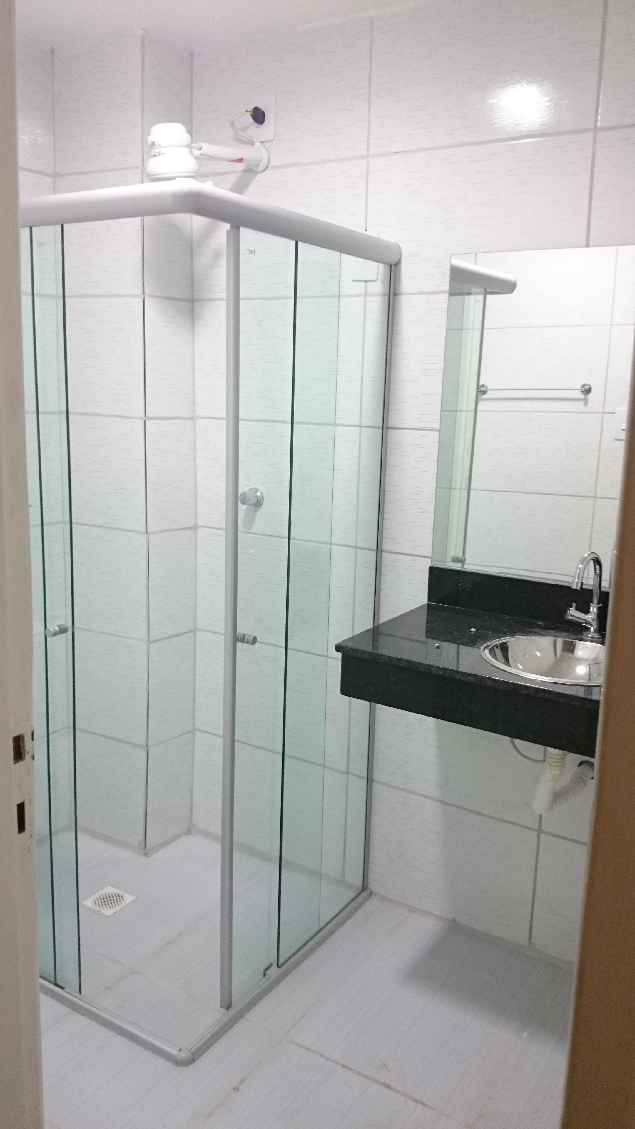 Un baño con ducha envuelta en vidrio, un lavamanos con espejo y paredes de azulejos.