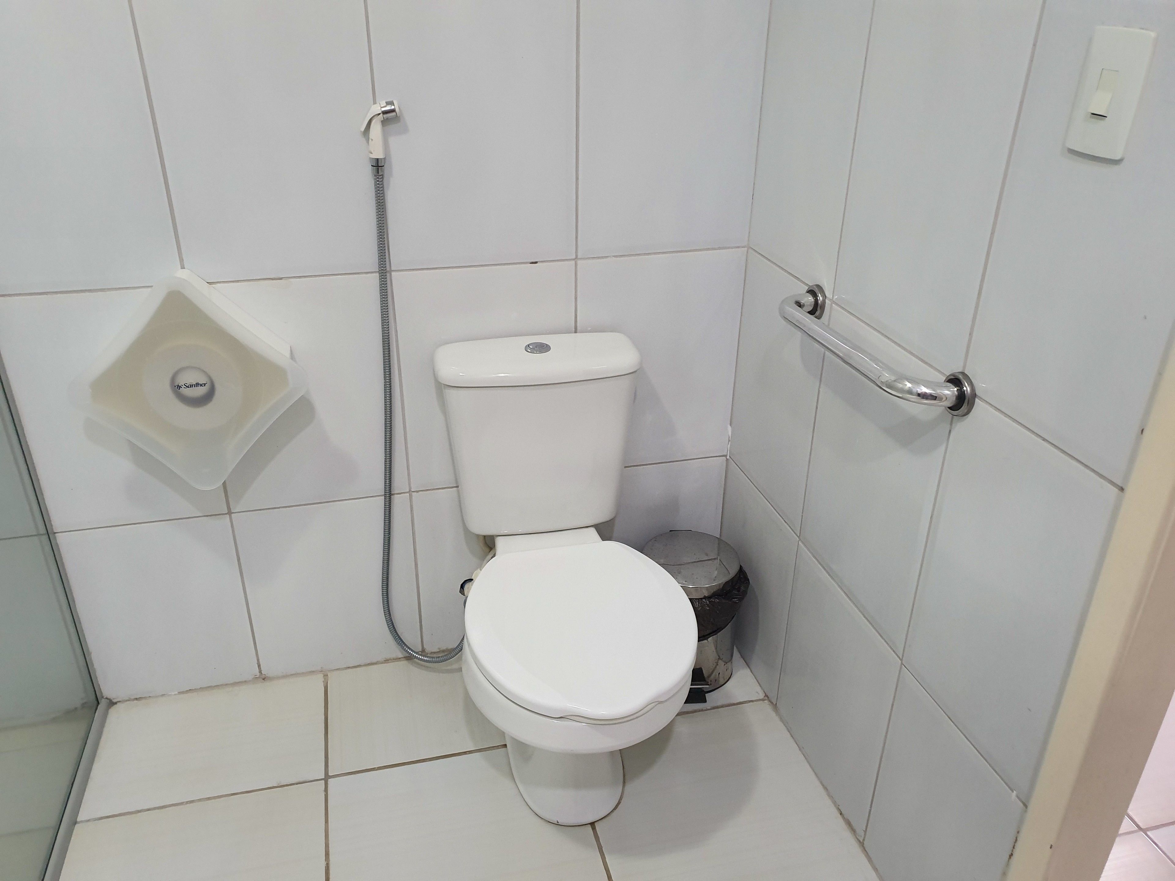 A small, white bathroom with a toilet, a handheld showerhead, and a bidet.