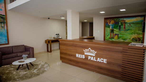 A reception desk labeled "REIS PALACE" with a painting of people in a field on the wall behind it. - Reis Palace Hotel (Petrolina)