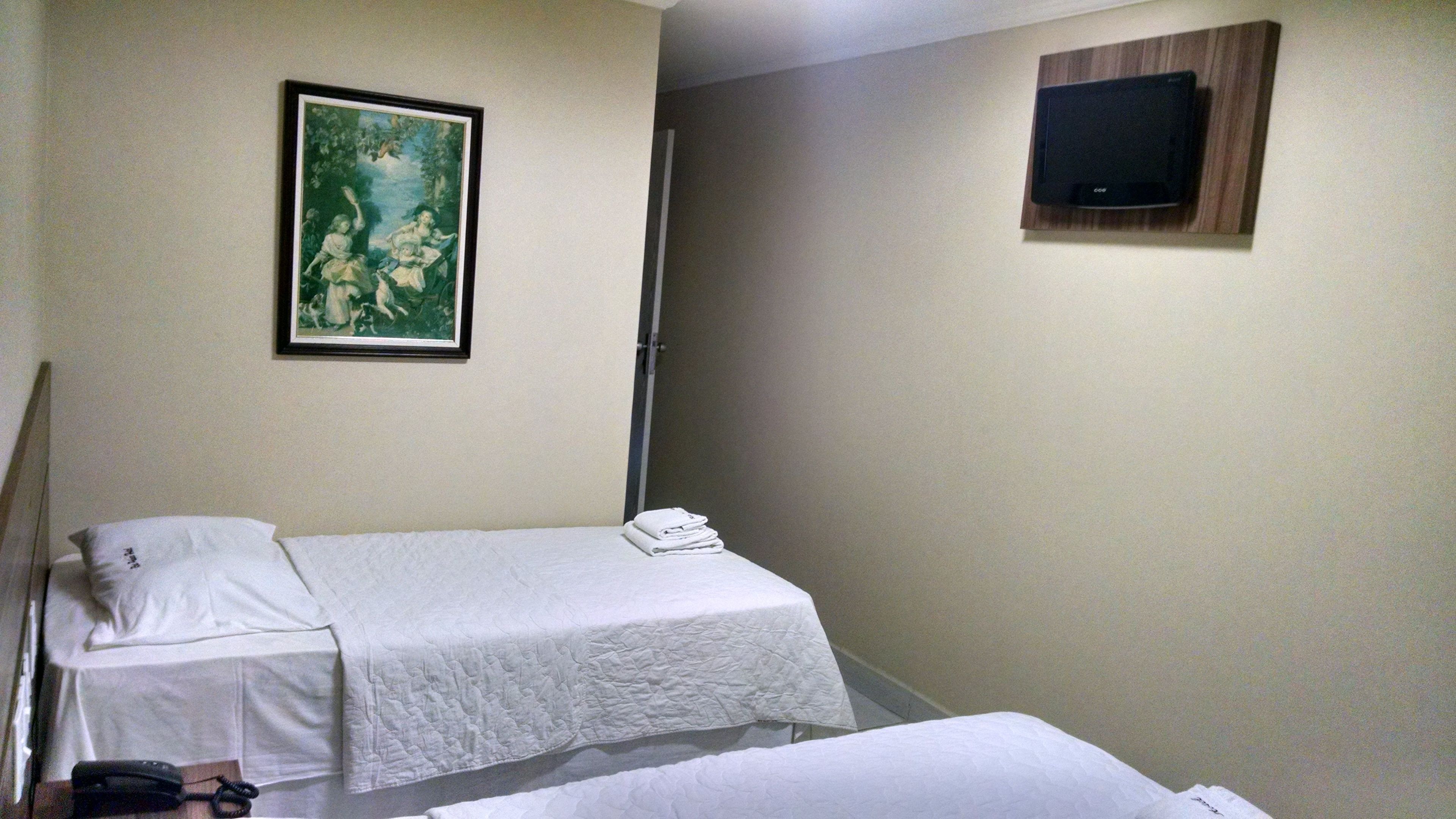 Habitación de hotel con dos camas individuales, un cuadro en la pared y un televisor fijado a la pared.