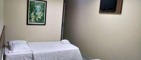 A hotel room with two single beds, a painting on the wall, and a television mounted on the wall.