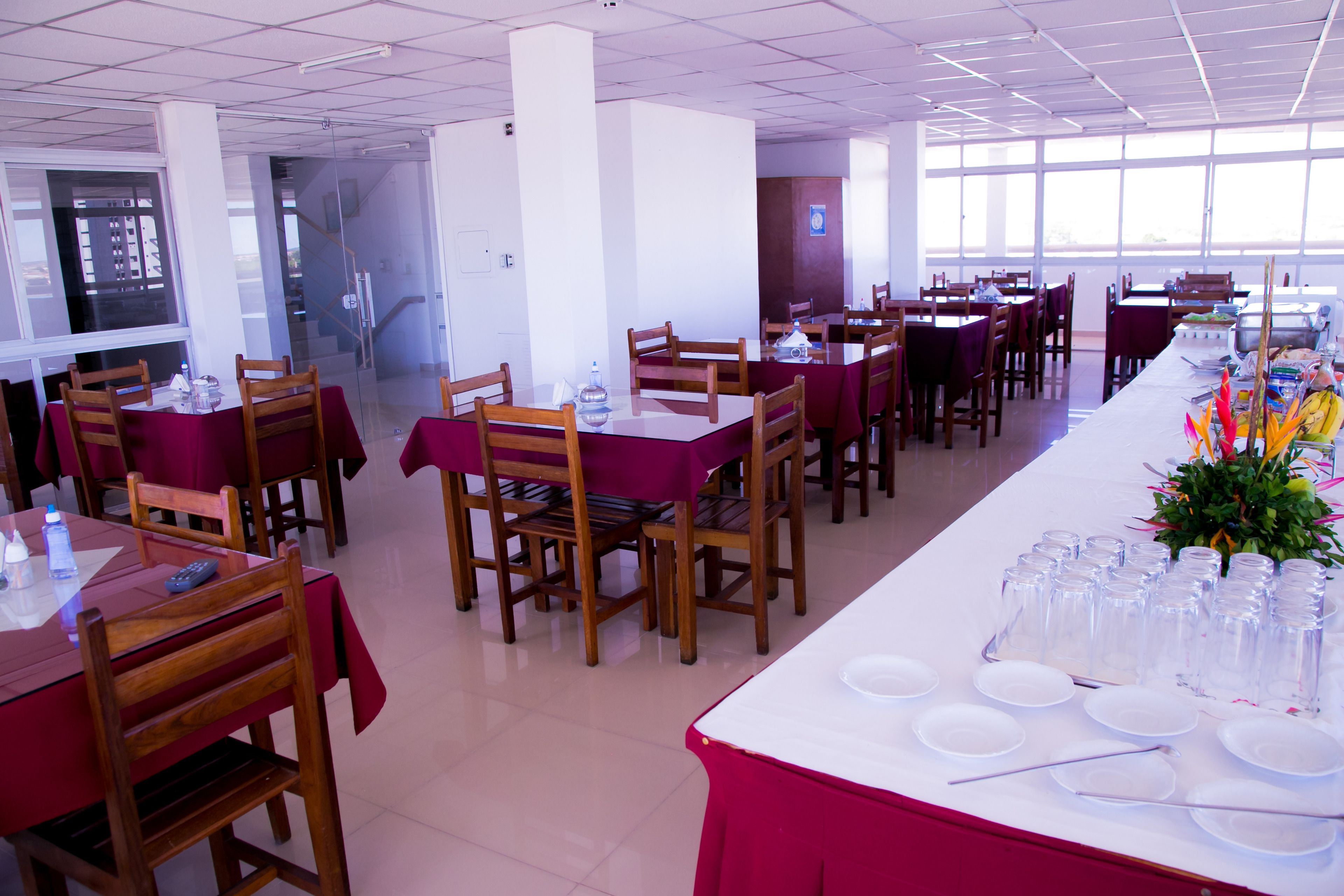 Uma sala ampla com grandes janelas, apresentando uma área de jantar com várias mesas e cadeiras.