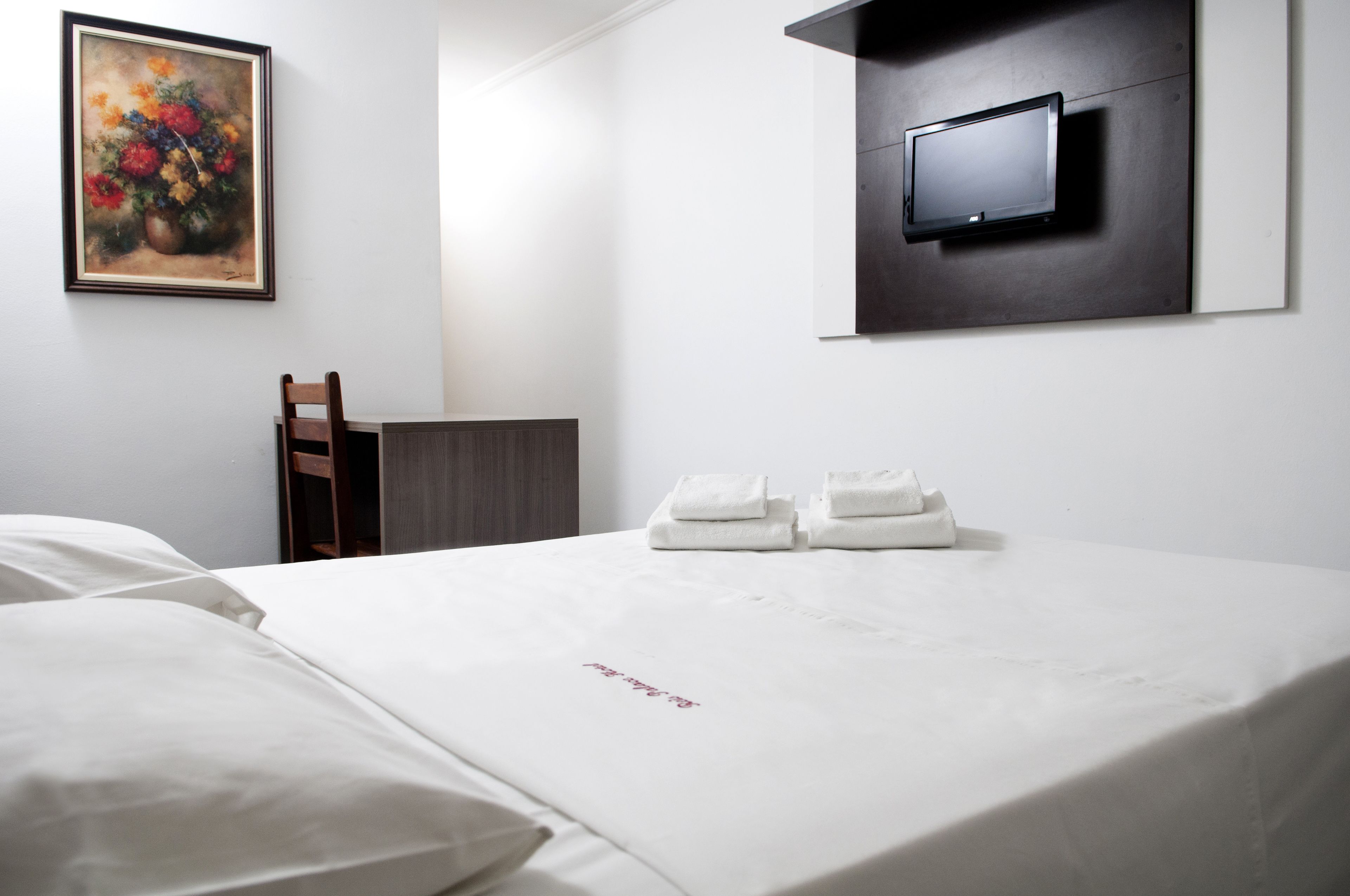Quarto de hotel com cama, televisão na parede e um quadro.