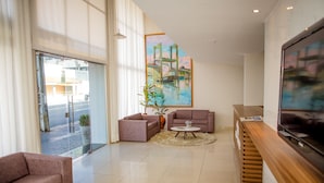 A modern hotel lobby with a large window, a painting of a bridge, a sofa, a coffee table, and a TV. - Reis Palace Hotel (Petrolina)