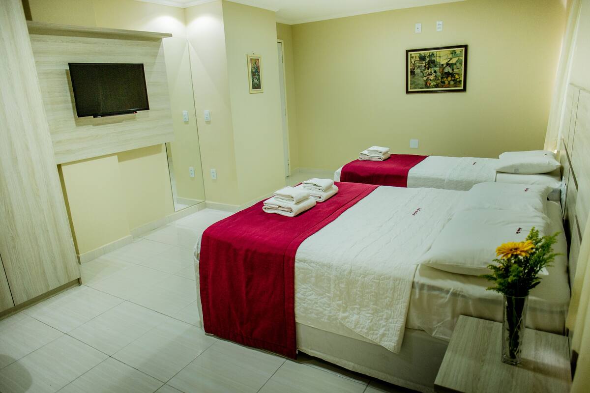 A hotel room with two beds, each with a red and white bedspread, and a flat-screen TV mounted on the wall.