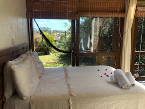 A bedroom with a large bed, a view of the outdoors, and a hammock. - Pousada Watu Kerere (Imbituba)