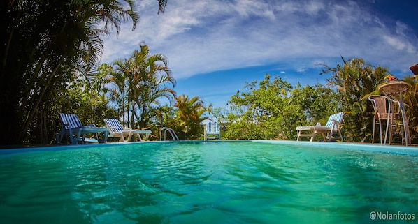 A clear pool with lounge chairs and a tropical setting.