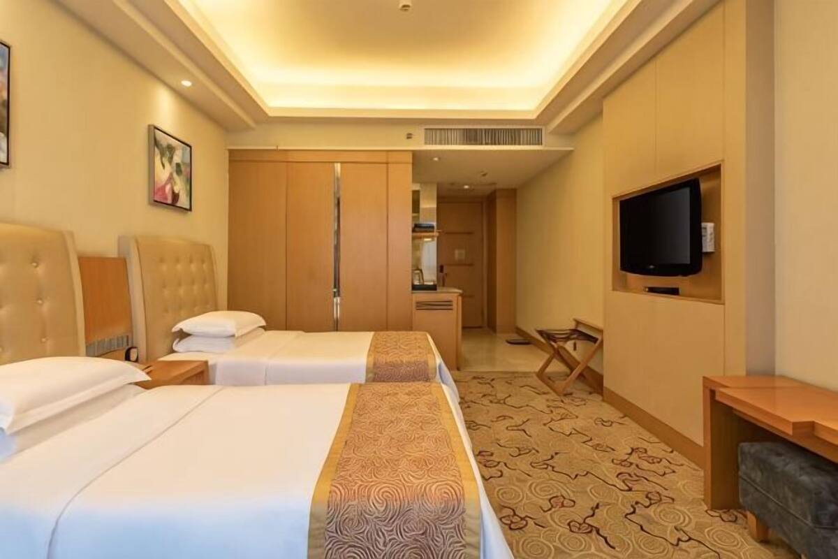 Habitació d'hotel amb dos llits, televisió, escriptori i petita cuina.