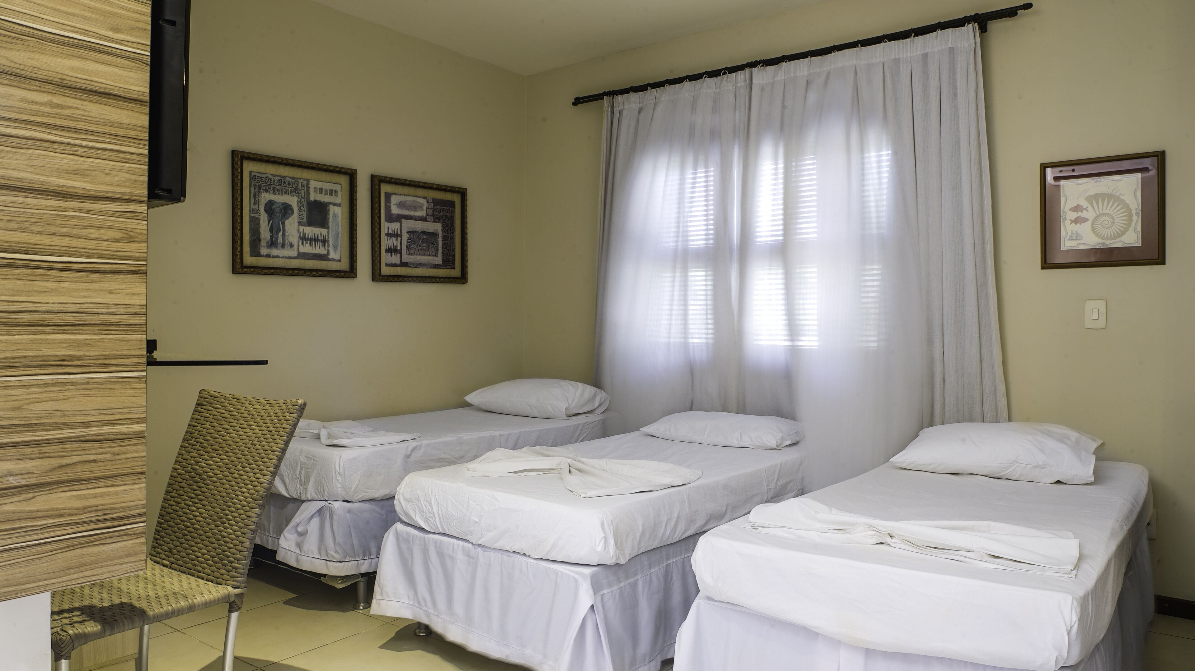 Una camera d'albergo con due letti singoli, una poltrona e due quadri appesi al muro.