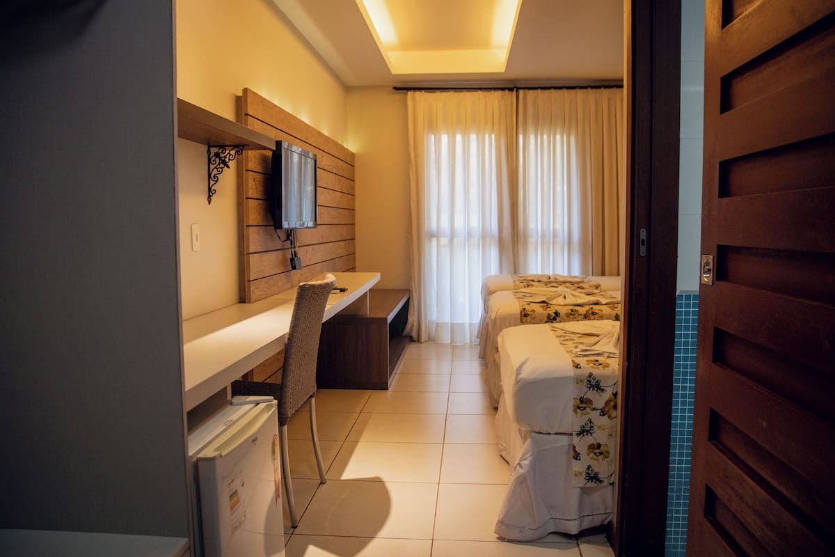 Habitación de hotel con escritorio, una silla, cama con ropa de cama floral y televisor montado en la pared.