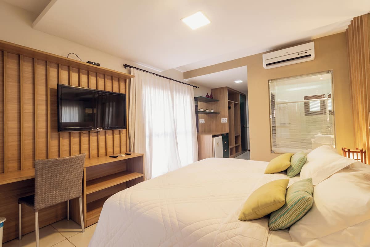 Una habitación de hotel con una cama, un televisor montado en la pared, un escritorio y una silla.