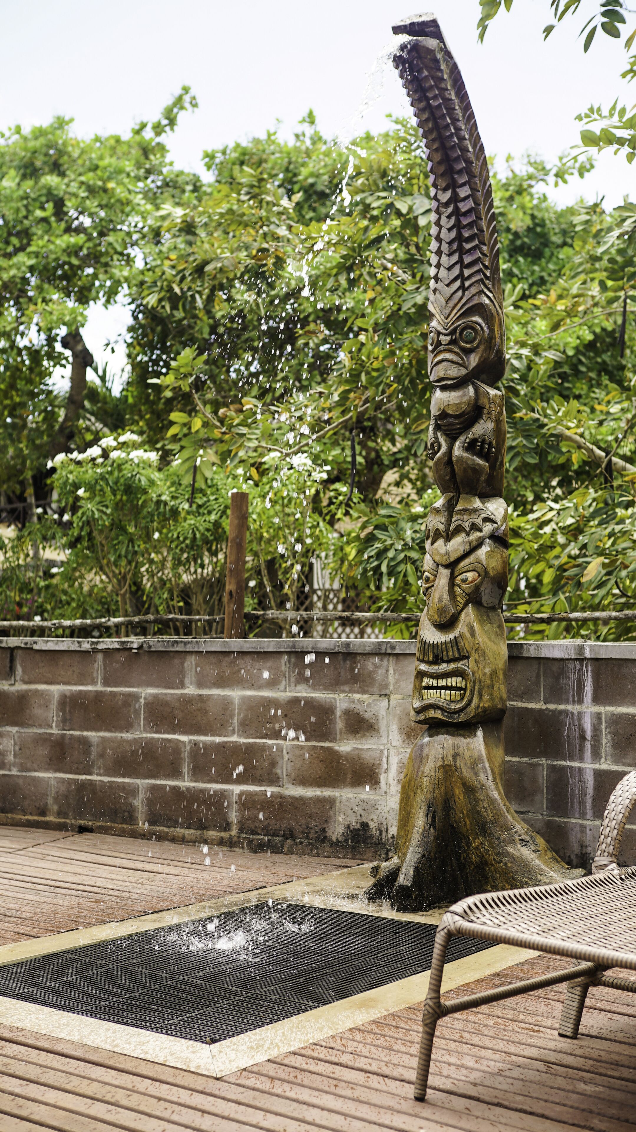 A wooden sculpture with a fish head and a human figure, surrounded by a water feature and a bench.
