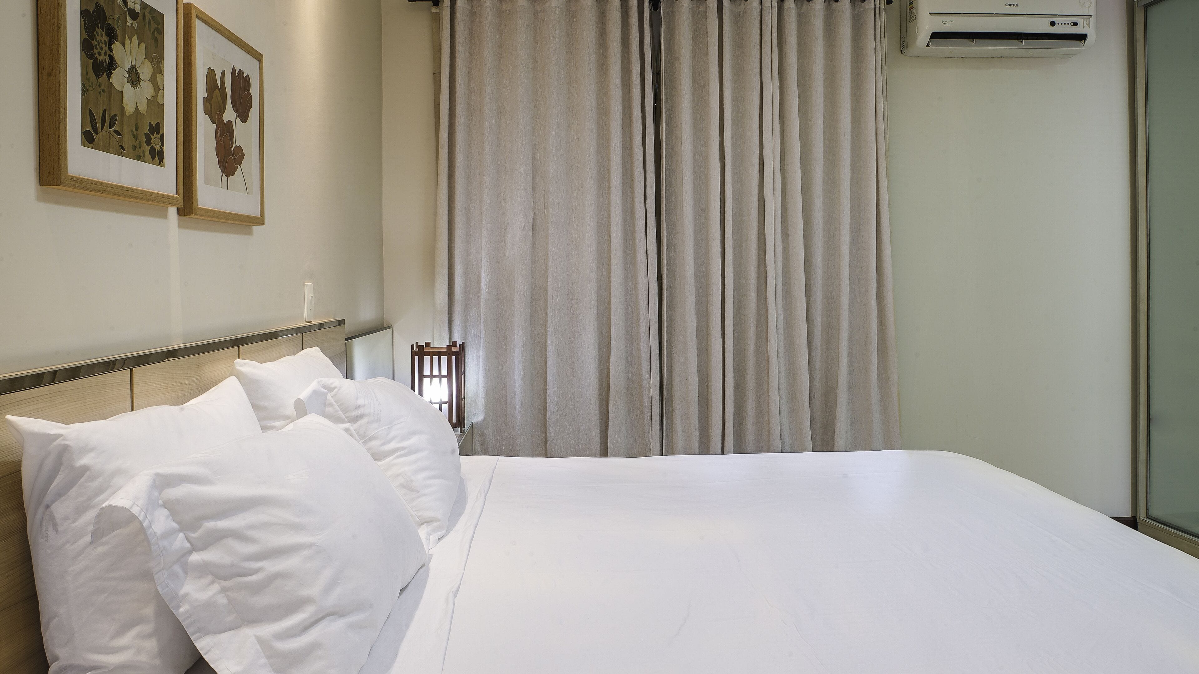 A hotel room with a large bed, white bedding, a wooden headboard, and a window with curtains.