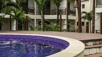 Una piscina con borde de azulejos, rodeada por una terraza de madera y palmeras.