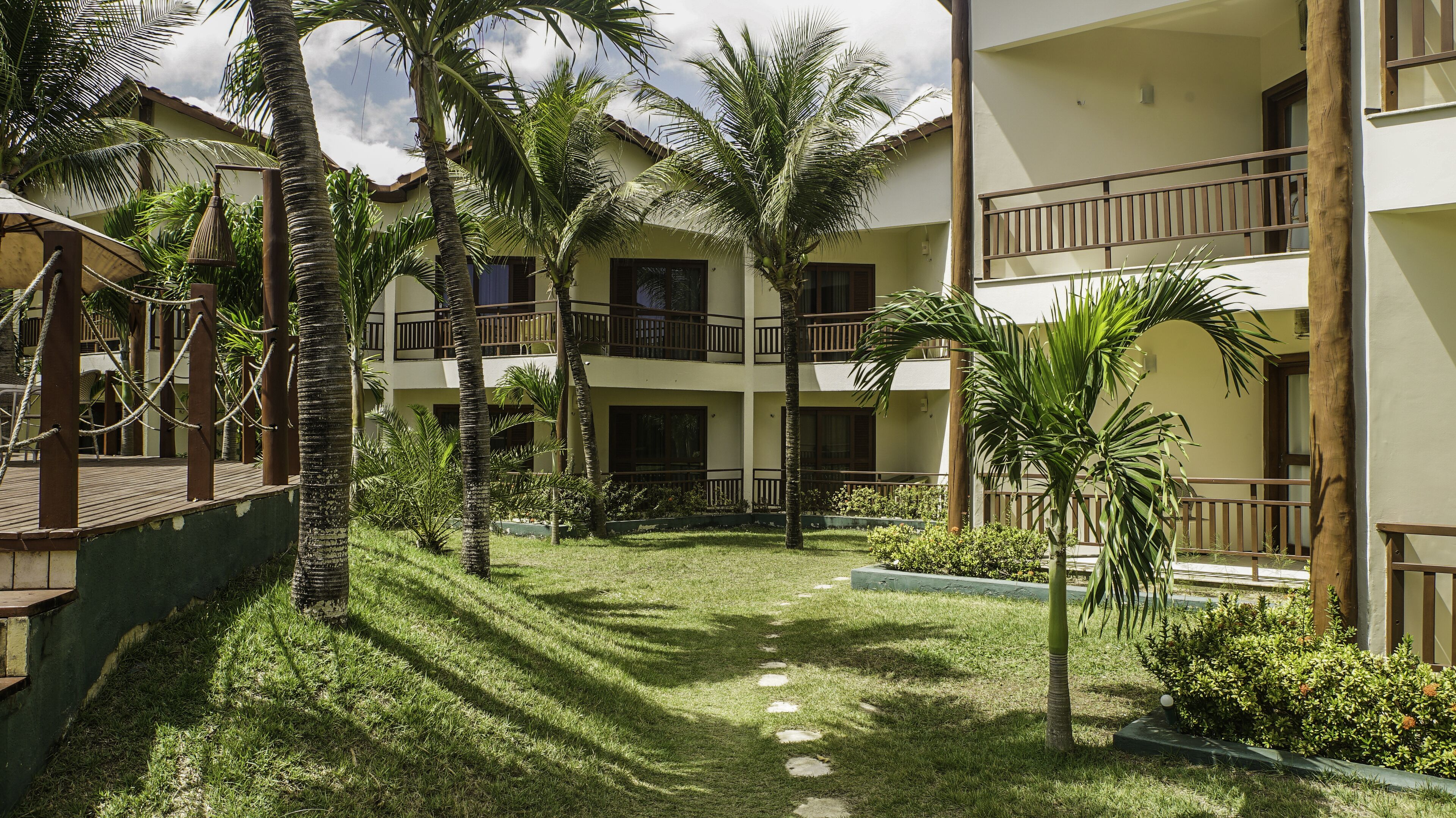 A courtyard with a central pathway, surrounded by palm trees and a building with balconies.