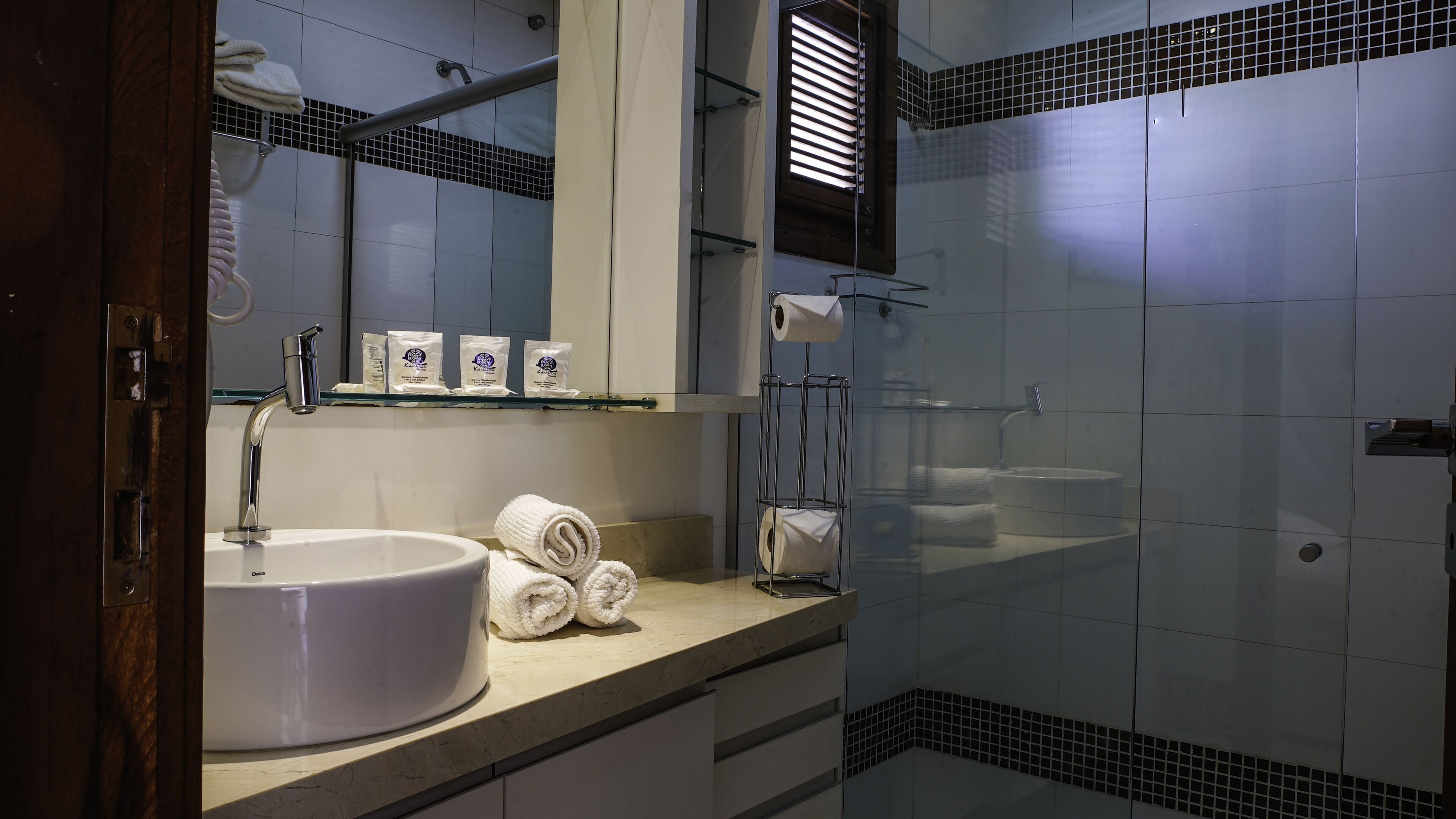 Un baño con lavamanos blanco, cabina de ducha con mampara de vidrio y espejo sobre el lavamanos.