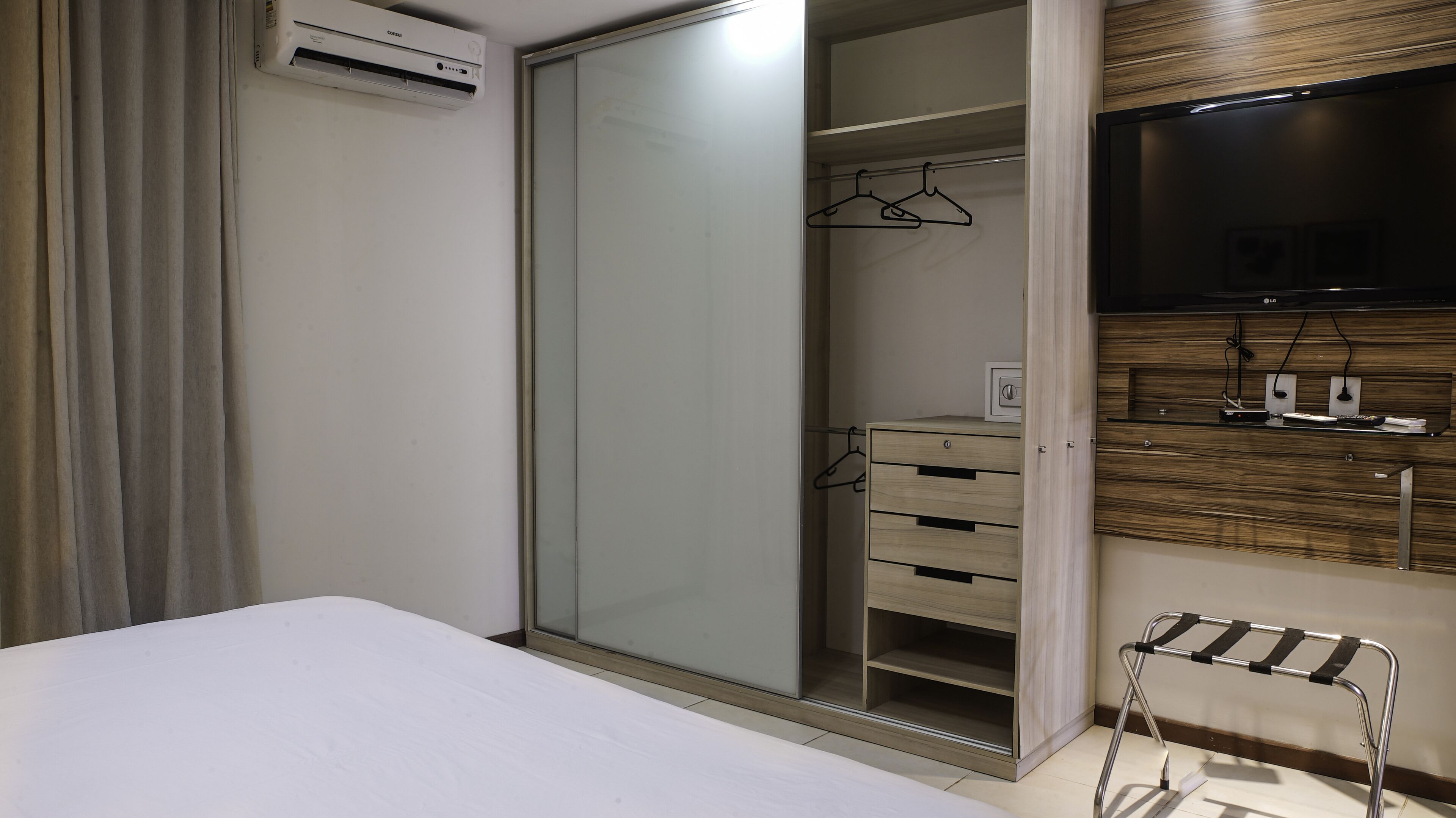 Une chambre à coucher avec un lit, une armoire avec un miroir, une télévision et une petite table avec un plateau.