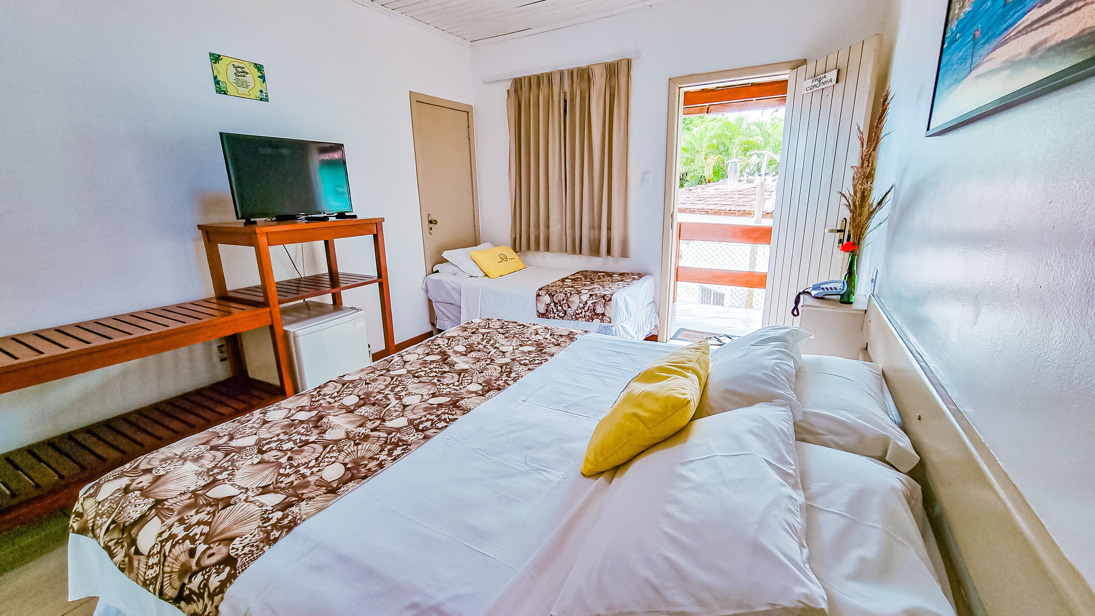 Une chambre d’hôtel avec deux lits, un téléviseur posé sur un meuble en bois, un petit réfrigérateur et une porte donnant sur un espace extérieur.