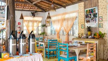 Un comedor rústico con mesas y sillas de madera, una estación de café y una pared decorada con cuadros enmarcados.