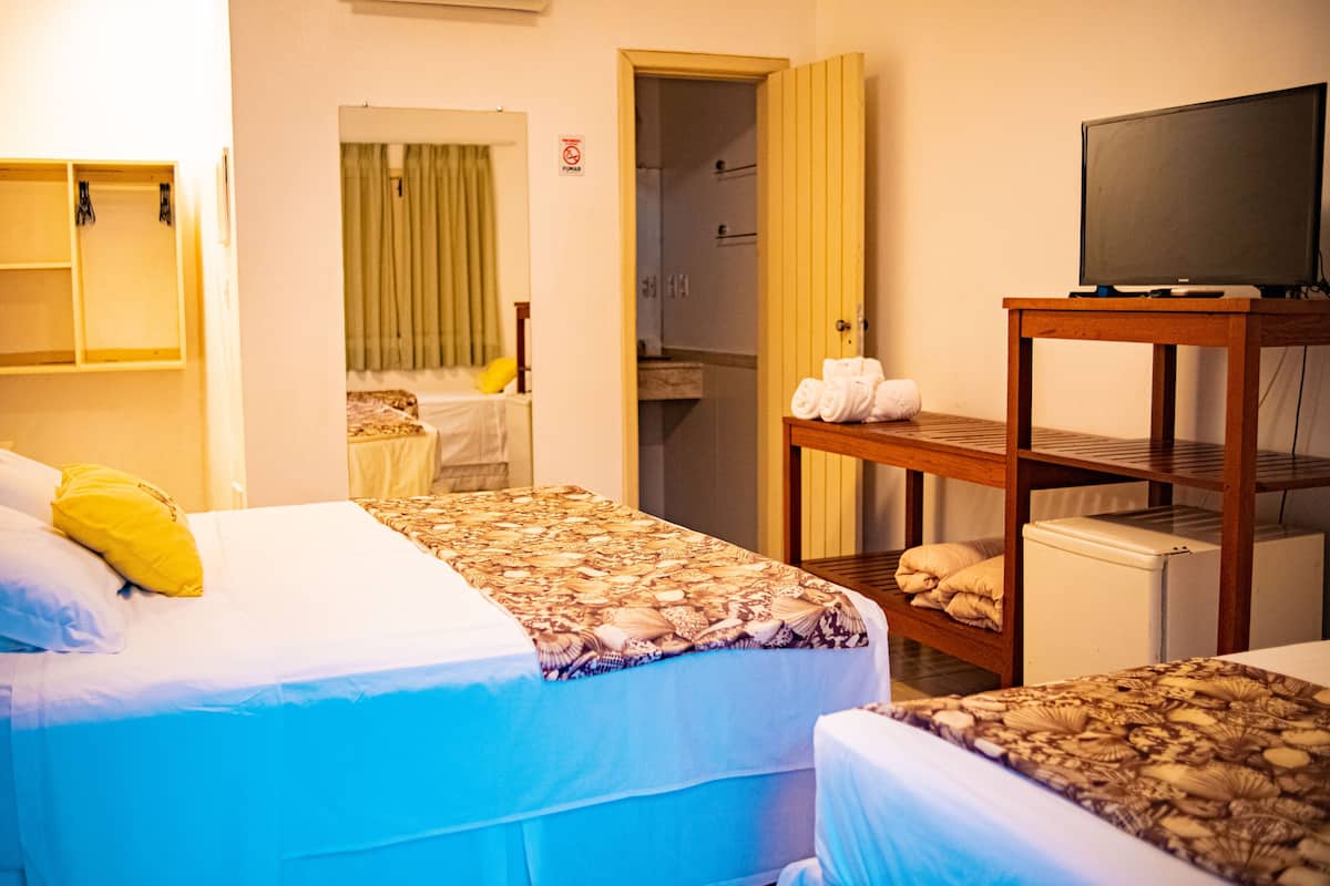 Ein Hotelzimmer mit zwei Betten, einem Fernseher auf einem Holzboden und einem durchgegangenen Tür zu sehendem Badezimmer.