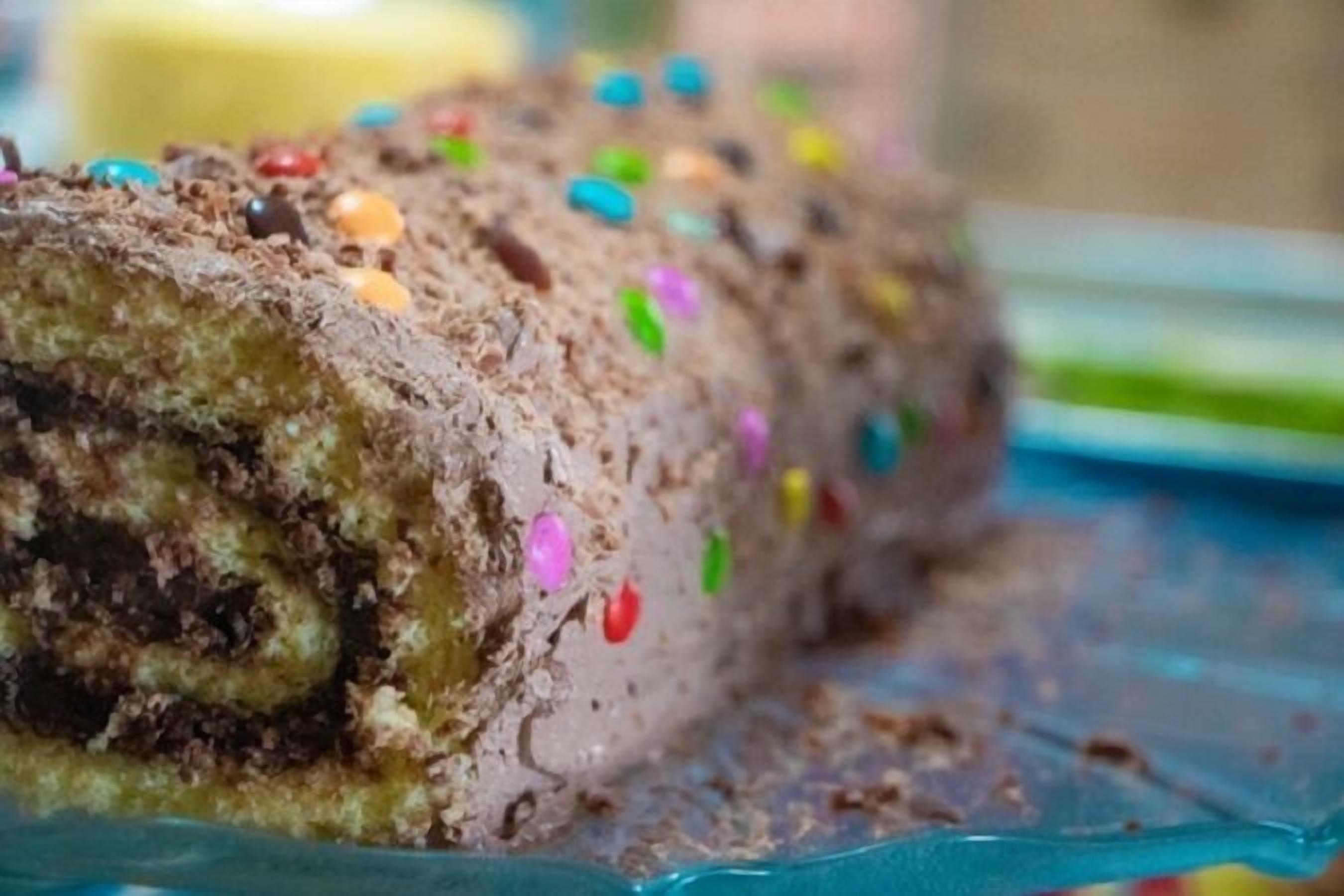 A chocolate roll with colorful sprinkles on a glass plate.