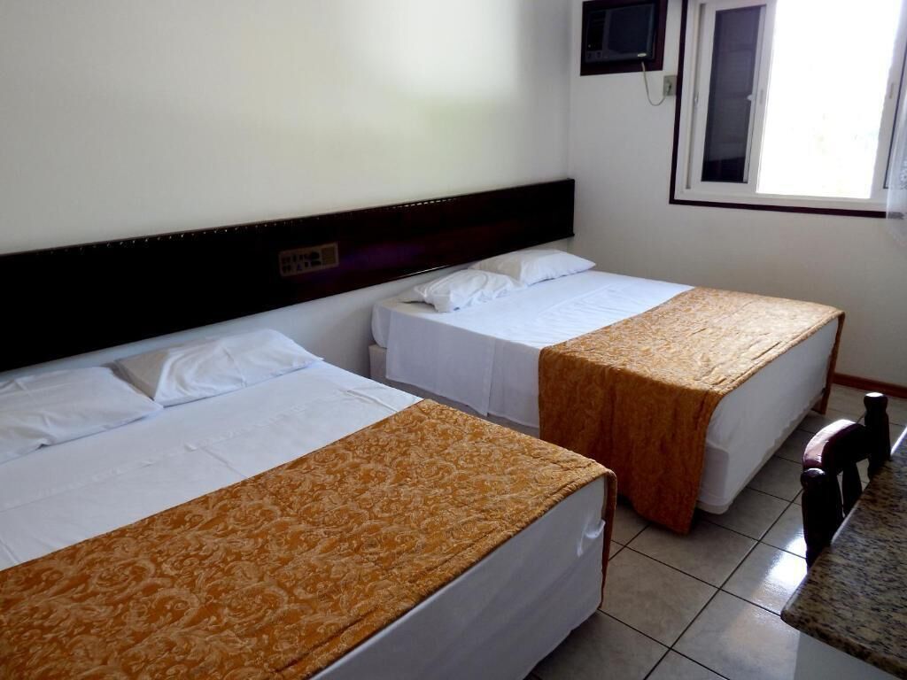 A hotel room with two single beds, a small table, and a TV mounted on the wall.