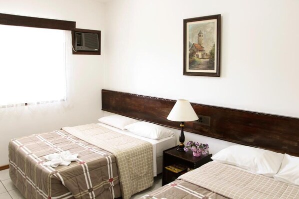 Habitación de hotel con dos camas, una mesita de noche con lámpara, un cuadro enmarcado en la pared y una ventana con persianas.