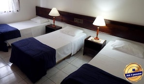 A hotel room with three single beds, each with a white mattress and blue bedspread. There are two bedside tables with lamps, and the room has a tiled floor. - Holz Hotel (Joinville)