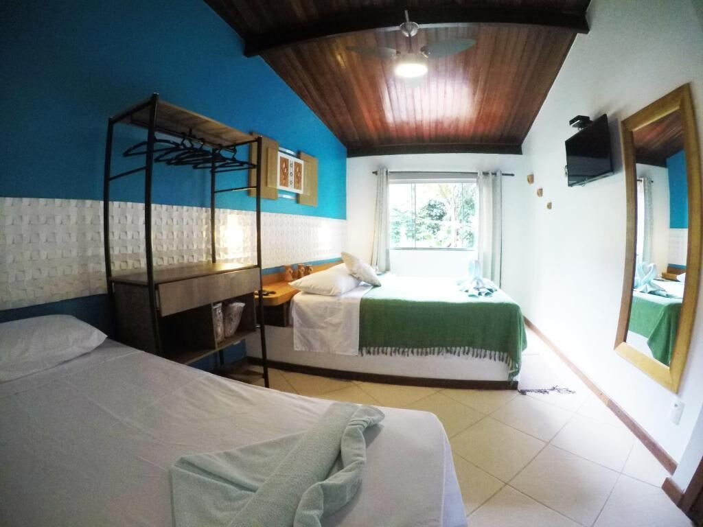 A room with two beds, a wooden ceiling, a window with curtains, and a mirror on the wall.