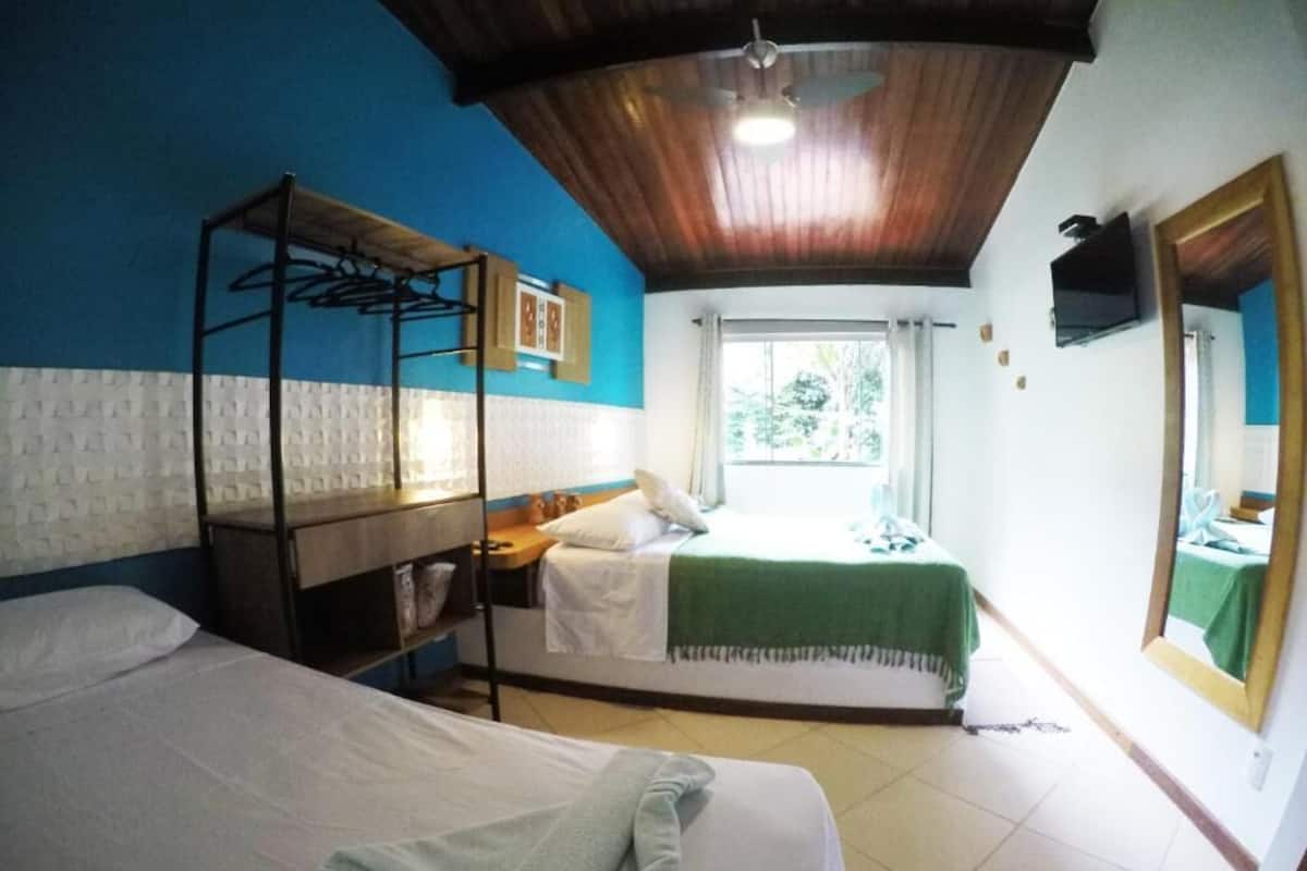 Una habitación con dos camas, techo de madera, ventana con cortinas y un espejo en la pared.