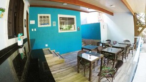 A restaurant with a blue wall, wooden ceiling, and a seating area with tables and chairs. - Pousada Guapuruvu (Angra dos Reis)