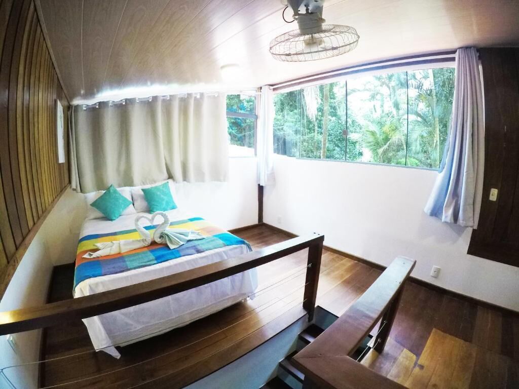 A room with a bed, a window with curtains, a ceiling fan, and a view of greenery outside.